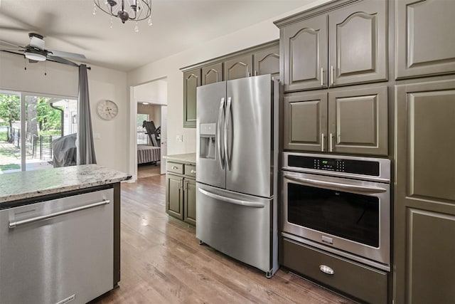 kitchen featuring light wood finished floors, appliances with stainless steel finishes, light stone counters, and ceiling fan with notable chandelier