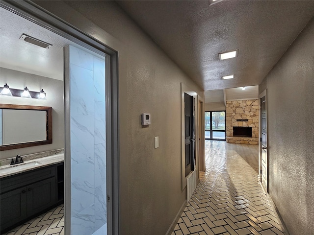 hallway with brick floor, a textured wall, a sink, and a textured ceiling