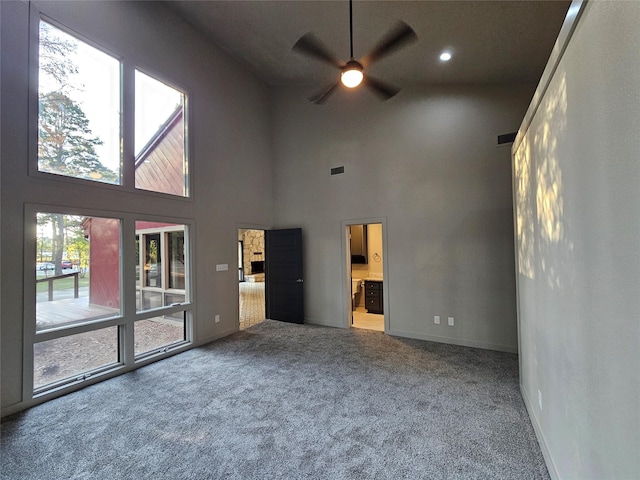 unfurnished living room featuring a high ceiling, ceiling fan, baseboards, carpet flooring, and visible vents