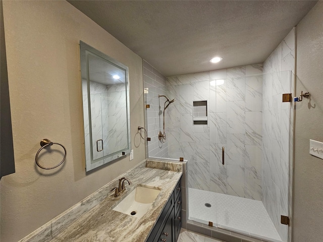 bathroom featuring a textured wall, a textured ceiling, vanity, and a marble finish shower