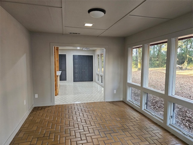 empty room featuring brick floor, visible vents, baseboards, and a wealth of natural light