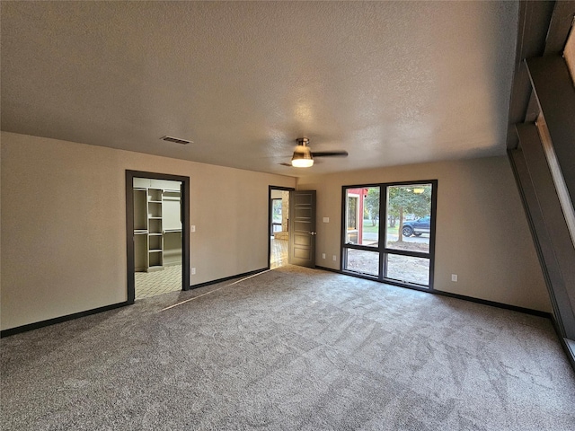 unfurnished room with a textured ceiling, carpet floors, visible vents, and baseboards
