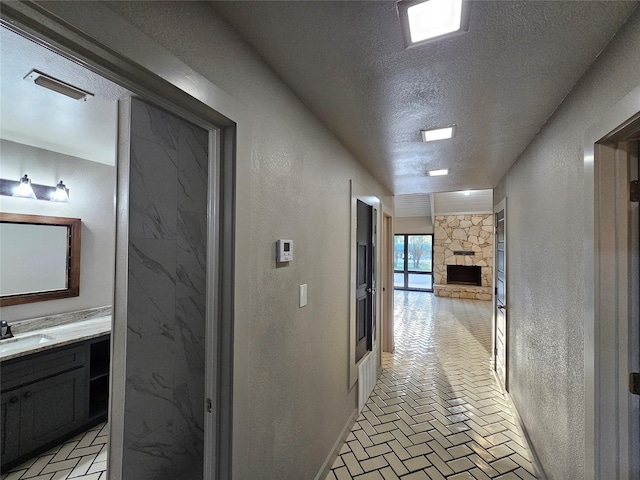 hall featuring a textured wall, a textured ceiling, brick floor, and a sink
