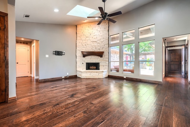 unfurnished living room featuring visible vents, wood finished floors, a stone fireplace, a ceiling fan, and a skylight