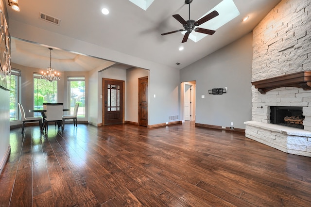 unfurnished living room with visible vents, a stone fireplace, dark wood finished floors, and ceiling fan with notable chandelier
