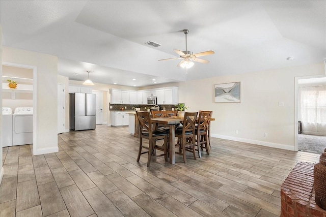 dining room featuring light wood finished floors, washing machine and dryer, vaulted ceiling, visible vents, and ceiling fan