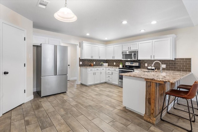 kitchen featuring white cabinets, a peninsula, a sink, visible vents, and appliances with stainless steel finishes