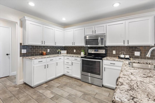 kitchen with white cabinets, stainless steel appliances, wood tiled floor, and a sink