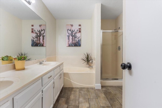 full bath with a shower stall, wood finished floors, double vanity, a sink, and a garden tub