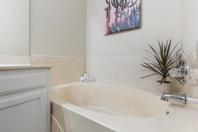 full bath with a textured wall, a garden tub, and vanity