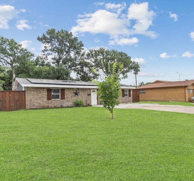 7025 Atha Dr, Dallas, TX 75217 - single story home with a front lawn, driveway, fence, brick siding, and roof mounted solar panels