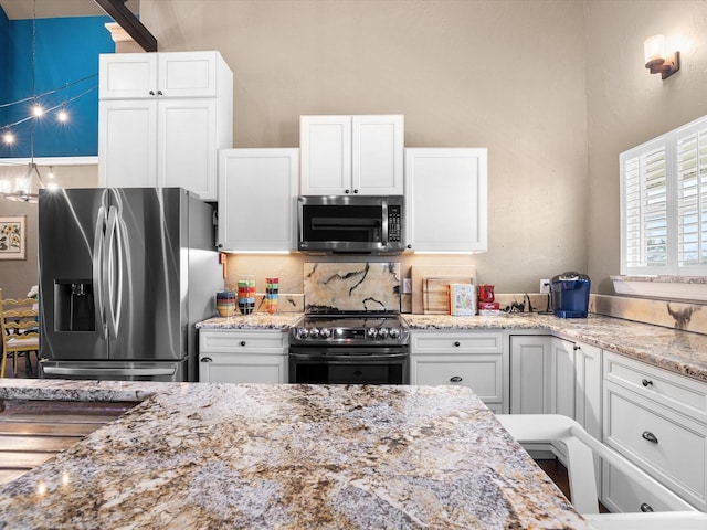 kitchen featuring white cabinets, stainless steel appliances, backsplash, a high ceiling, and light stone countertops