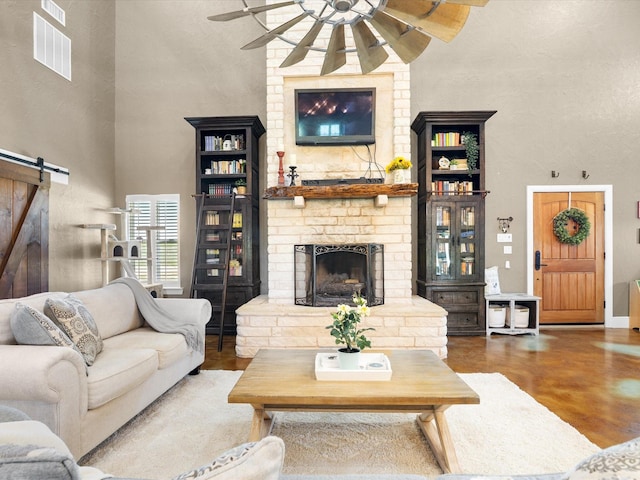 living area with a barn door, a towering ceiling, concrete flooring, ceiling fan, and a fireplace