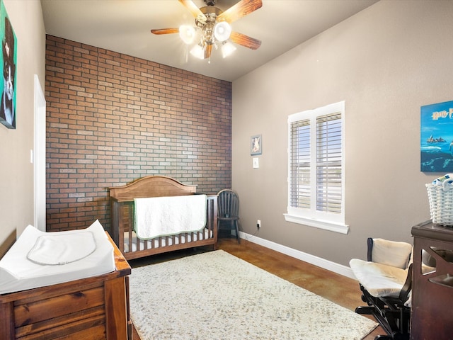 bedroom featuring brick wall, a ceiling fan, baseboards, and a nursery area