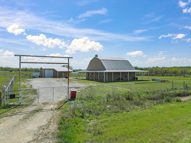 view of front of home featuring dirt driveway, a gate, fence, an outdoor structure, and a garage