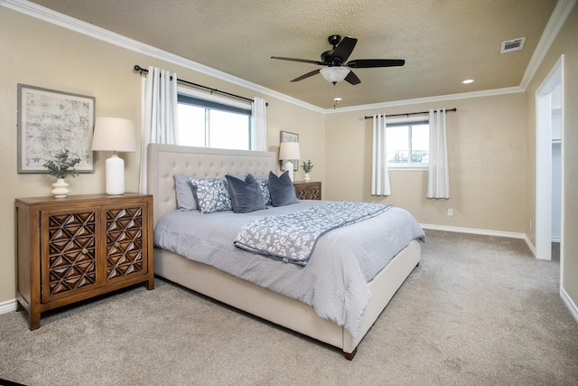 carpeted bedroom featuring a ceiling fan, a textured ceiling, baseboards, ornamental molding, and visible vents