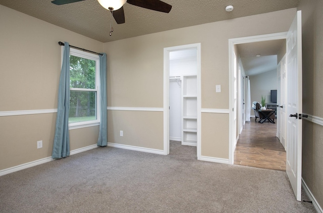unfurnished bedroom featuring a spacious closet, carpet floors, baseboards, a textured ceiling, and ceiling fan