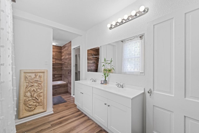 full bathroom with a garden tub, wood finished floors, a sink, and double vanity
