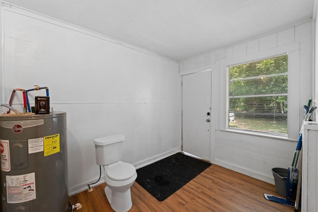 bathroom featuring wood finished floors, crown molding, toilet, and electric water heater