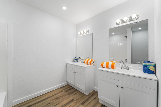 bathroom featuring baseboards, wood finished floors, two vanities, and a sink