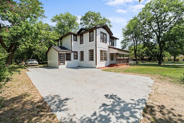 back of house featuring concrete driveway, a yard, and covered porch