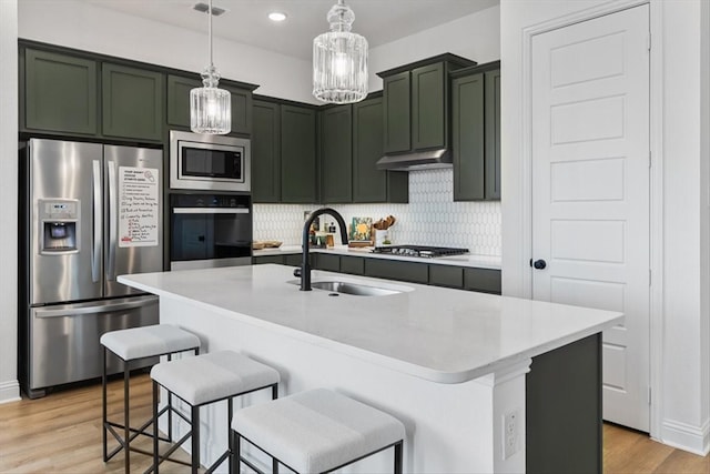 kitchen with stainless steel appliances, a sink, light wood-type flooring, green cabinets, and under cabinet range hood