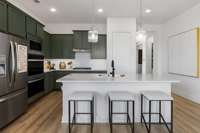 kitchen featuring stainless steel appliances, a kitchen breakfast bar, a sink, green cabinets, and under cabinet range hood