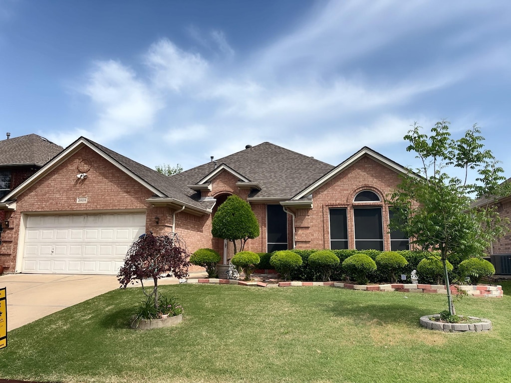 single story home featuring a front lawn, driveway, a shingled roof, a garage, and brick siding