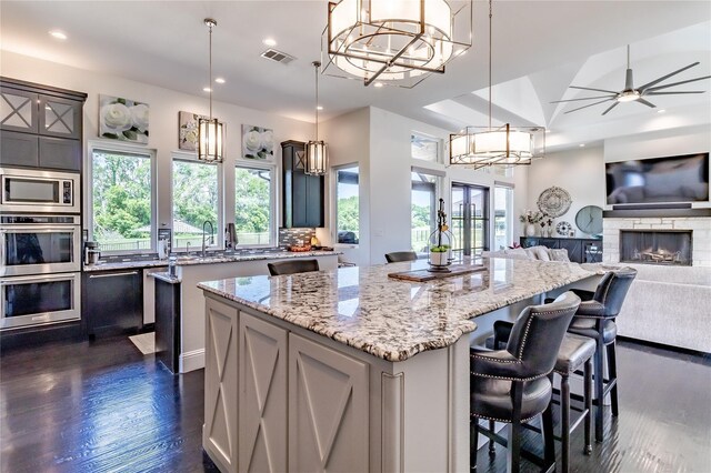 kitchen with light stone counters, a notable chandelier, dark wood finished floors, wine cooler, and a kitchen island