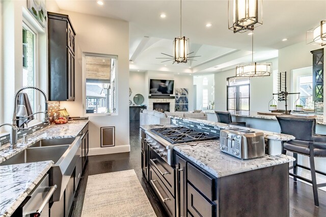 kitchen featuring decorative backsplash, hanging light fixtures, dark wood finished floors, a sink, and ceiling fan with notable chandelier