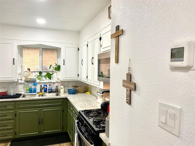 kitchen featuring stainless steel microwave, green cabinets, a sink, white cabinetry, and range with gas stovetop