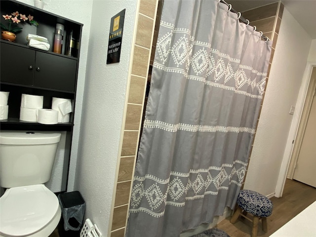 full bathroom featuring wood finished floors, toilet, a shower with curtain, and a textured wall