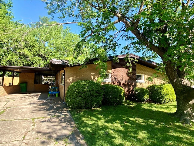 view of side of home with driveway, a lawn, and brick siding