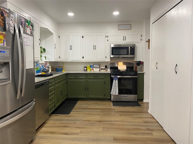 kitchen with light wood-style flooring, appliances with stainless steel finishes, light countertops, green cabinets, and white cabinetry