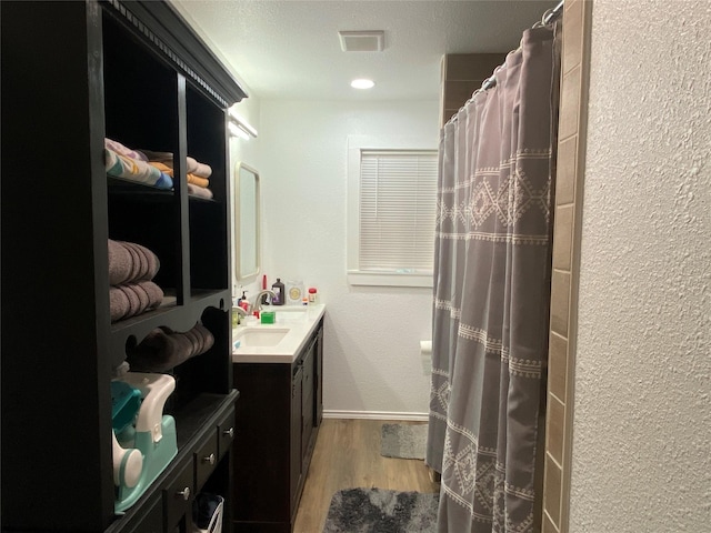 bathroom with a textured wall, visible vents, a shower with shower curtain, wood finished floors, and vanity