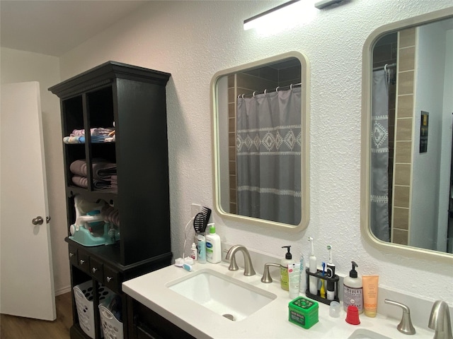 bathroom featuring wood finished floors, a shower with shower curtain, a textured wall, and vanity