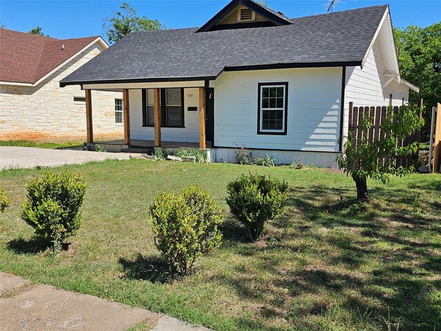 view of front of home featuring fence, a porch, a shingled roof, and a front yard