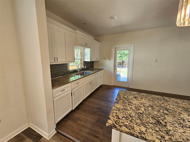 kitchen featuring dark wood-style flooring, dark stone countertops, a sink, and white cabinetry
