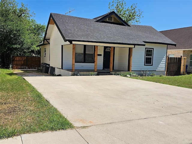 view of front of home featuring roof with shingles, driveway, covered porch, and fence