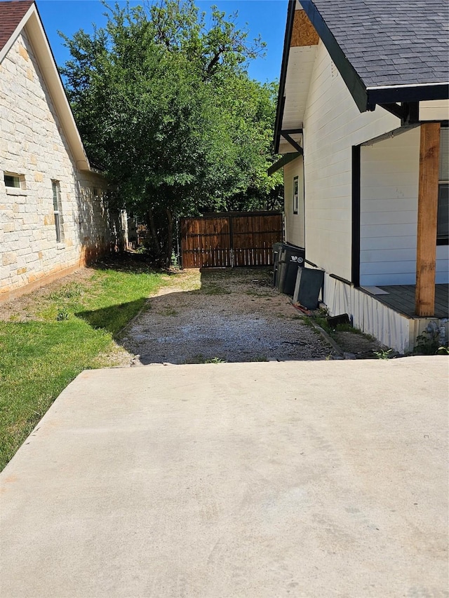 view of side of property featuring fence, stone siding, and a shingled roof