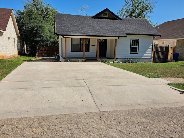 bungalow-style home featuring a porch, a front yard, fence, and a shingled roof