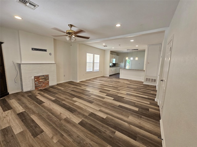 unfurnished living room featuring a fireplace, visible vents, dark wood-style floors, and ceiling fan