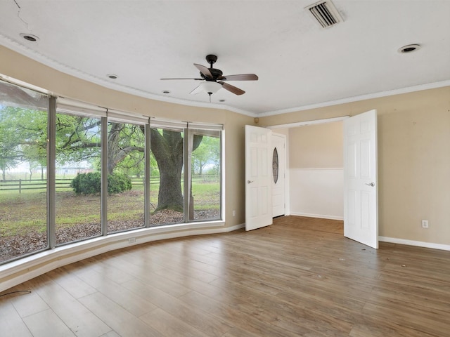 empty room featuring visible vents, baseboards, ornamental molding, wood finished floors, and a ceiling fan