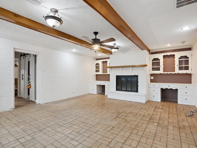 unfurnished living room with visible vents, beam ceiling, a fireplace, a ceiling fan, and brick floor