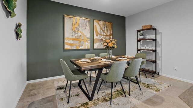 tiled dining area featuring baseboards and an accent wall