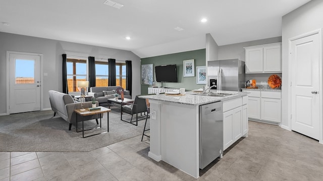 kitchen featuring white cabinets, a sink, a center island with sink, open floor plan, and appliances with stainless steel finishes
