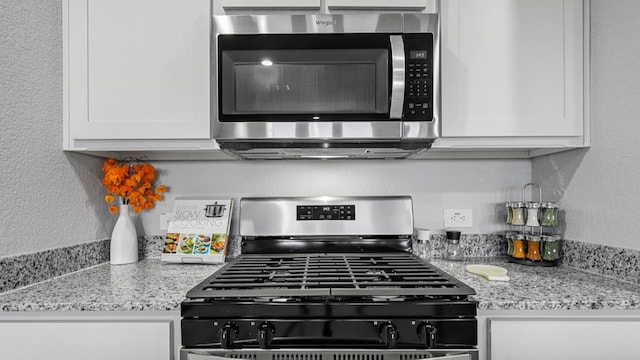 kitchen featuring light stone counters, white cabinets, a textured wall, and stainless steel appliances