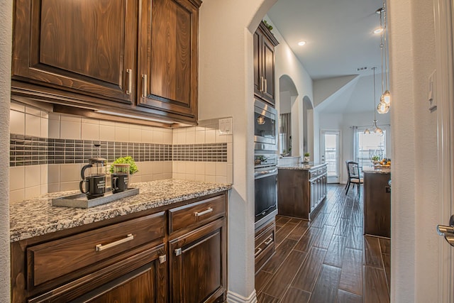 kitchen featuring arched walkways, backsplash, light stone countertops, and appliances with stainless steel finishes