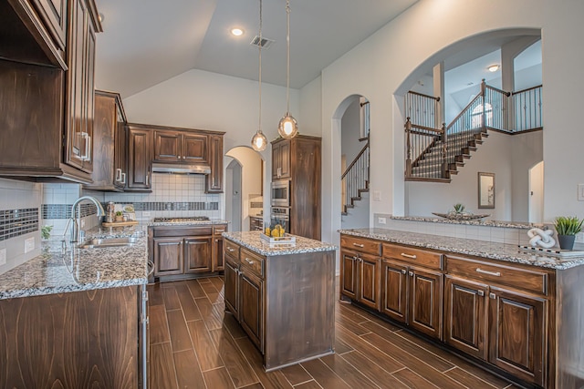 kitchen with arched walkways, a sink, under cabinet range hood, a kitchen island, and appliances with stainless steel finishes