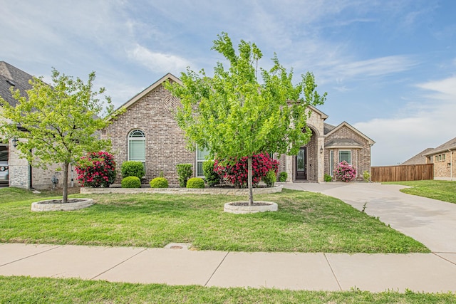 view of property hidden behind natural elements featuring fence, a front lawn, and brick siding
